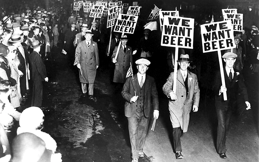 Black-and-white photo of anti-prohibition demonstrators walking with signs that say 'We want beer', while a crowd watches.